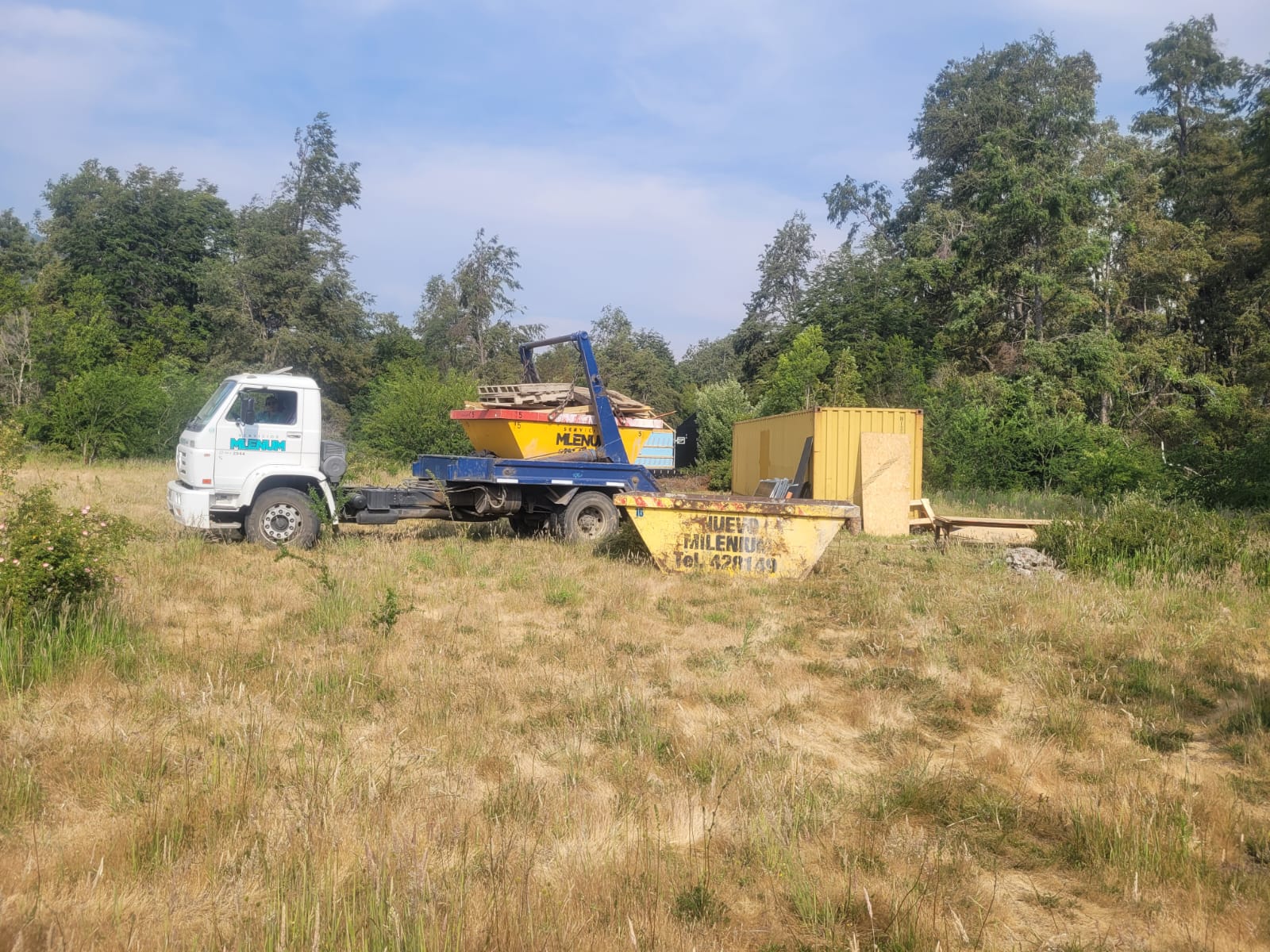 Camión y volquetes de Milenium trabajando en un terreno rodeado de bosque