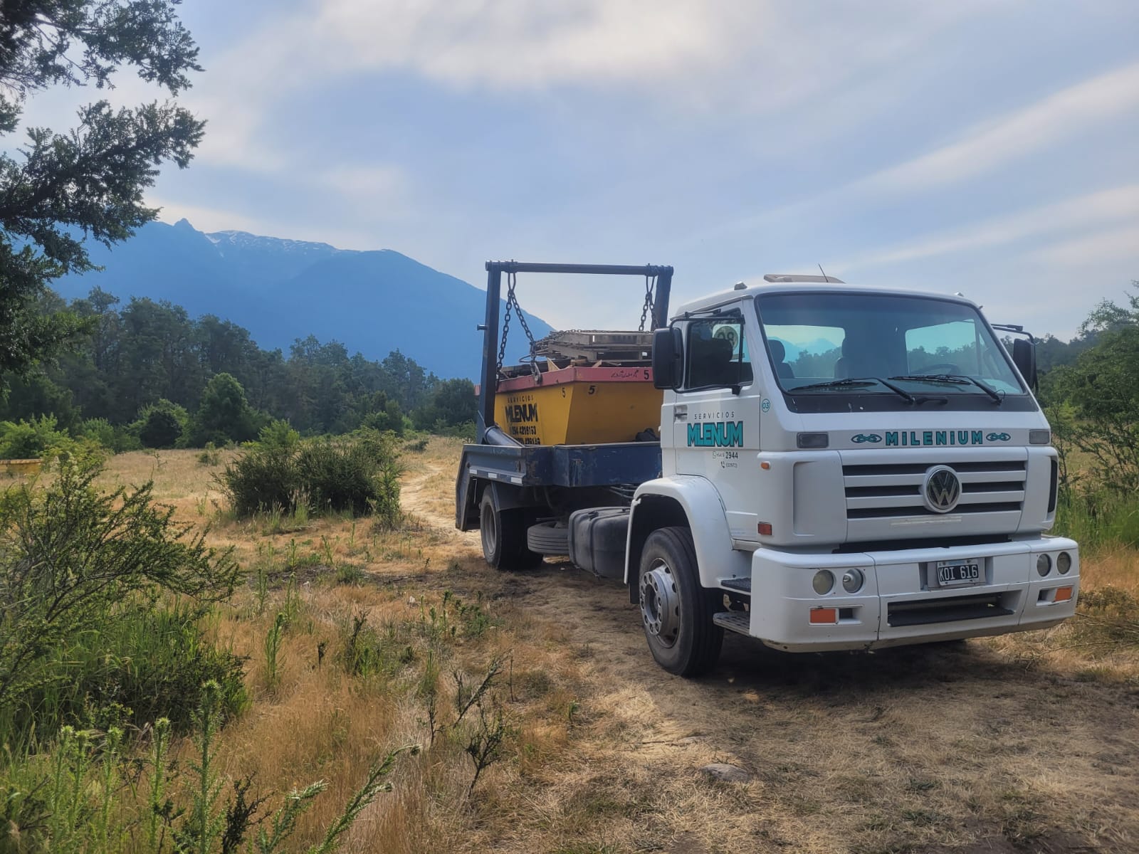 Camión de Milenium Volquetes transportando un contenedor con un cerro nevado de la cordillera de fondo
